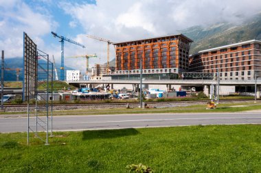 Dağlık Andermatt köyünde şantiyesi olan turizm beldesi; Canton Uri; mavi bulutlu bir yaz gününde. Fotoğraf 21.08.2024; Andermatt; İsviçre. Arka planda birçok vinç; şimdilik; büyük bir inşaat alanı, ama gelecekte; 