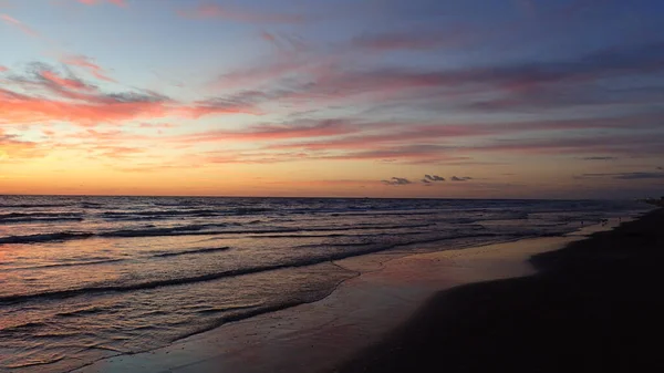 Sahilde gün doğumu, güneş soldan batıyor, açılı dalgalar.