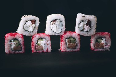 Kadın eli, Kaliforniya suşi rulolarını Çin çubuklarıyla alır. Seçici odak, siyah arkaplan.