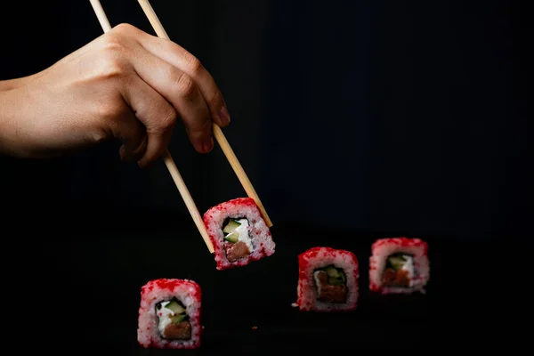 Female hand takes california sushi rolls with Chinese chopsticks. Selective focus, black background.