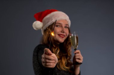 beautiful sparklers and a glass of champagne in a woman hands on gray background. Looks and smiles into the camera, isolated on gray background..