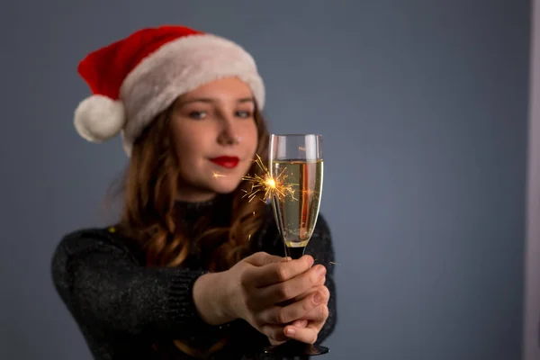 beautiful sparklers and a glass of champagne in a woman hands on gray background. Looks and smiles into the camera, isolated on gray background..