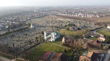 Gündoğumunda Katolik kilisesi ve mezarlığının üzerinde insansız hava aracı uçuşu. Sombor, Sırbistan, Avrupa. 4K