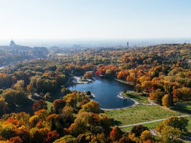 Göl ve sonbahar parkının üzerinde arka planda gökdelenler olan insansız hava aracı uçuşu. Mont-Royal Parkı, Montreal, Kanada