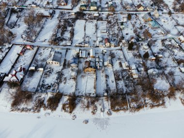 Kış boyunca Kazakistan 'ın Uralsk kentindeki donmuş nehrin yakınındaki karla kaplı evlerin hava manzarası. c.