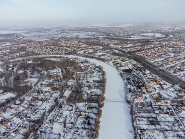 Kış boyunca Kazakistan 'ın Uralsk kentindeki donmuş nehrin yakınındaki karla kaplı evlerin hava manzarası. c.