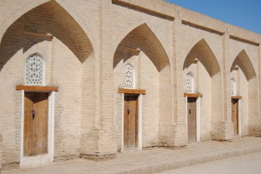 Güneş altında ahşap kapılar ve pencereler, Özbekistan 'ın Khiva kentindeki bir medresede kemerli tuğla girişler.