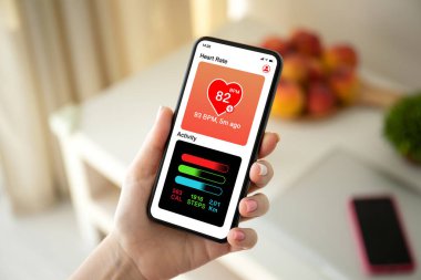 female hand holding phone with app heart and activity on the screen background of room in house