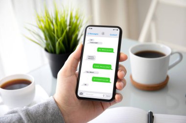 male hands holding phone with app messenger on the screen over a table in office