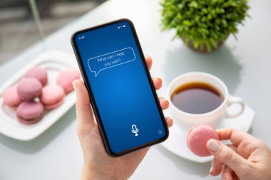 female hands holding phone  with app personal assistant on the screen over table with dessert and coffee in summer cafe