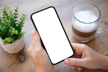 Kadın elleri kafedeki masanın izole ekran arka planına sahip telefonu tutuyor.