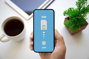 eSim 'de Sim kartının değiştirildiği telefonun erkek eli ofisteki masanın ekranında.  