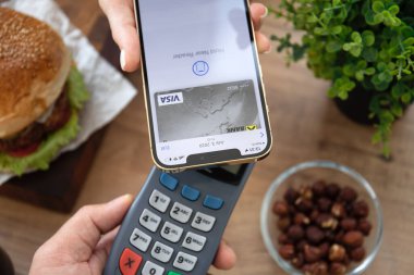Alanya, Türkiye - 23 Eylül 2021: Ekranda Raiffeisenbank uygulamalı Apple iPhone 'u tutan ve POS terminali üzerinden ödeme yapan kadın kafede Burger satın aldı