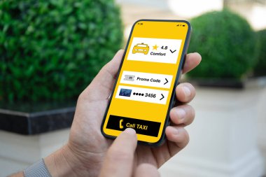 Adam elinde telefonla taksi çağırma başvuru ekranı ile caddede bekliyor.