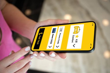 Kadın, sokak lambasının arka planında taksi çağırma uygulaması bulunan telefonu tutuyor.