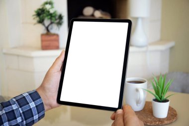 Kır evindeki şöminenin arka planında izole ekranı olan bilgisayar tabletini tutan erkek elleri