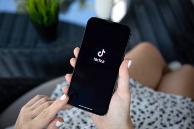 Alanya, Türkiye - 5 Ekim 2023: Ellerinde Apple iPhone 14 Pro Max ile ekranda canlı yayın yapan servis medyası ve video TikTok olan kadın elleri.