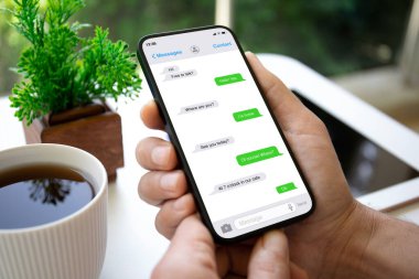Adam bir kafede ekranın arkasındaki masada uygulamalı kurye ile telefonu bekletiyor.