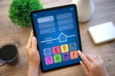 Kadın elleri bilgisayar tabletini, uygulamalı akıllı ev ile birlikte apartmanlardaki masanın ekran arka planında tutuyor