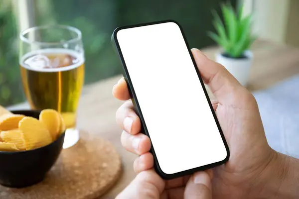 stock image Man hand hold phone with isolated screen background of table with beer and chips in caf