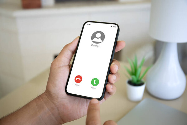 Мужчина держит в руках телефон с входящим звонком на экранном фоне квартиры в доме