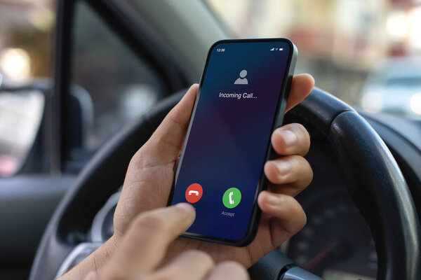 Man hand hold phone with incoming call on screen background of steering wheel in car