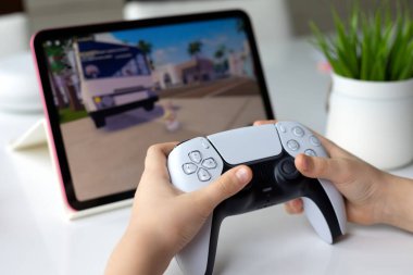 Alanya, Türkiye - 11 Nisan 2024: DualSense kablosuz denetleyici PlayStation 5 ve Apple iPad Air ile ekrandaki Roblox mobil oyunu IOS tabletinde çocukların elleri.