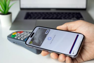Alanya, Türkiye - 4 Nisan 2024: Apple iPhone 15 Pro Max ve Apple Pay Raiffeisenbank uygulaması ekranda ve POS terminal kıyafetlerini mağazadan satın almak için çevrimiçi geçiş kartı.