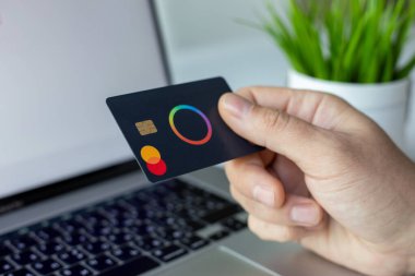 Alanya, Türkiye - 4 Nisan 2024: Erkek el ele tutuşan plastik kart Payonetici Mastercard ve dizüstü bilgisayar Macbook çevrimiçi POS terminal ödeme kartı 