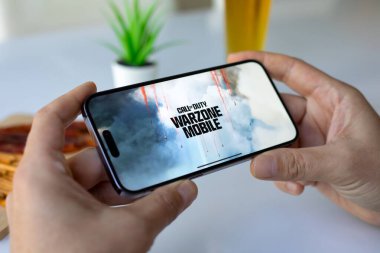 Alanya, Turkey - May 3, 2024: Man hands holding phone Apple iPhone 15 Pro Max with game Call of Duty Mobile in the screen. Games Call of Duty was created by the Activision Publishing, inc. clipart