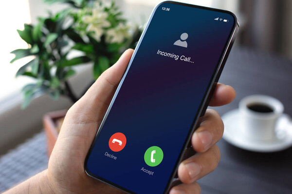 мужчина держит телефон с входящим звонком на экране стола с кофе в офисе