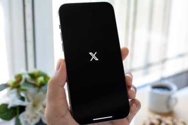 Alanya, Türkiye - 12 Temmuz 2024: İnsan eli iPhone 15 Pro Max ile sosyal ağ habercisi X Twitter ekranda.