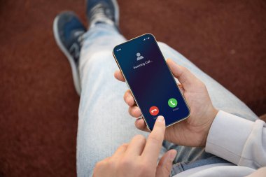 Erkek eli telefonu tutuyor ve ekranda kot pantolon ve spor ayakkabıları görünüyor.