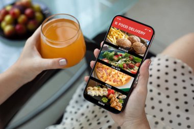 Kadın eli, ekrandaki kafenin arka planında yemek dağıtım uygulaması olan telefonu tutuyor.