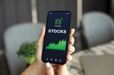 Ofisteki perde arkası masasında hisse senedi alım satım uygulaması olan bir kadın el telefonu.