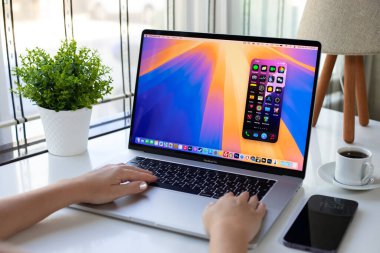 Alanya, Türkiye - 25 Eylül 2024: Elma Macbook Pro ve iPhone 15 Pro Max Mirroring ile ekranda AI Apple Intelligence Siri ve IOS Sequoia 18 ile el ele tutuşan kadın.