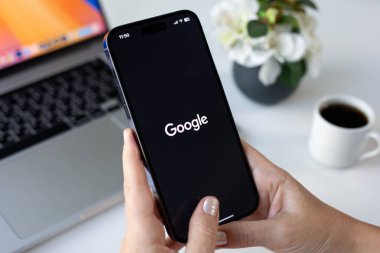 Alanya, Türkiye - 25 Eylül 2024: Elma iPhone 15 Pro Max ve MacBook ile sosyal ağ servisi Google 'ı ekranda tutan kadın eli.