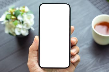 Kafe masasının arka planında tek ekran görüntüsü olan erkek eli telefonu.