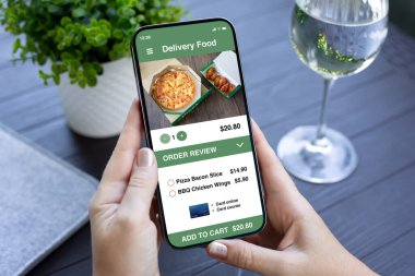 Kadın eli, ekrandaki kafeterya arka planında yemek dağıtım uygulaması olan telefonu tutuyor.