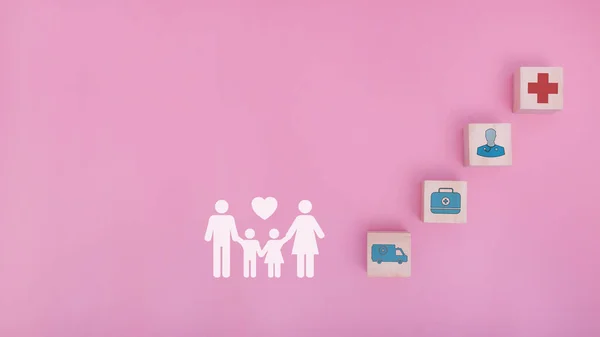 Family with insurance for your health concept. Wooden blocks with healthcare medical icons and family icons on pink background, copy space.