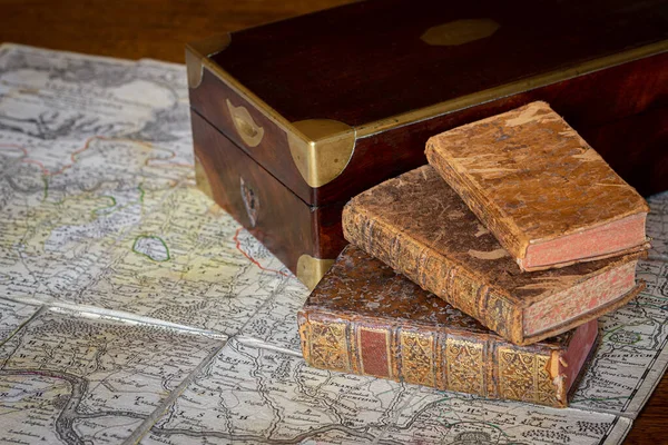 Pile of antique books with a leather cover and golden ornaments, close to a wooden box on an ancient topographic map