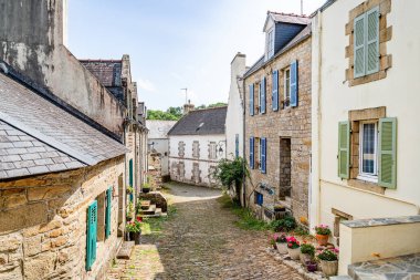 Güneşli bir kaldırım taşı caddesi Fransa 'nın Brittany kentindeki Pont-Croix' da eski taş evler, yemyeşil alanlar ve çiçek açan bitkiler arasında esiyor..