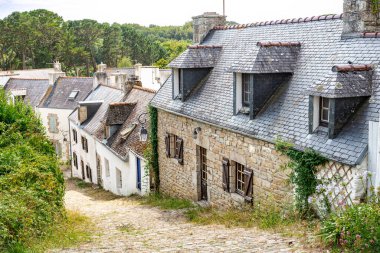 Güneşli bir kaldırım taşı caddesi Fransa 'nın Brittany kentindeki Pont-Croix' da eski taş evler, yemyeşil alanlar ve çiçek açan bitkiler arasında esiyor..