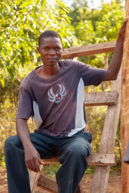 Xai Xai, Mozambik, Nisan 2014: Yetimler için yeni bir ev inşa eden bir merdivenin üzerinde oturan genç ve fit Afrikalı bir adam veya genç adam.