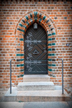 Süslü demir tokmaklı ahşap kapı, renkli tuğlalarla dolu kemerli giriş ve menteşeler küçük bir kilise, kilise, kale veya devlet binasının olası yan girişi. Arap ya da Asyalı etkisi değil.