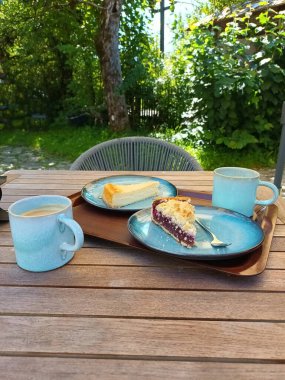 Cheesecake, kirazlı kek ve bahçede bir masada iki kahve fincanı.