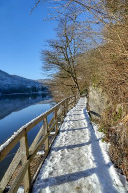Eifel bölgesindeki Heimbach 'taki Rur yakalama havzasının kenarındaki tırabzanlarla karlı yürüyüş yolu.