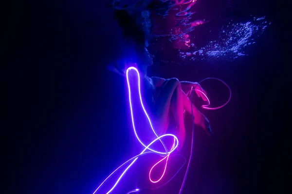 Gymnast shows underwater performance in neon light. Soft blurred focus