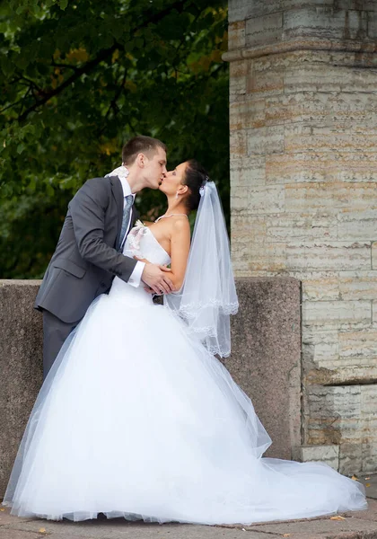 白いウェディングドレスの花嫁は鉄のフェンス 緑の葉の近くに立つ — ストック写真