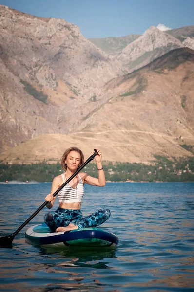 stock image Girl rides a SUP board on the river on mountains background